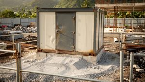 Module de stockage sécurisé en métal sur un chantier en Martinique, porte renforcée et zone d’accès stabilisée en gravier compacté.