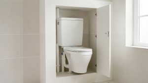 Toilettes modernes avec tuyaux dissimulés dans un coffrage en placo démontable, doté d’un panneau d’accès légèrement ouvert.