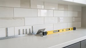 Installation d’une nouvelle crédence directement sur un carrelage existant dans une cuisine, avec outils et matériaux de rénovation visibles.