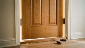 Porte d’entrée en bois légèrement désalignée après des travaux, frottant contre le seuil avec ses charnières et un tournevis visibles.